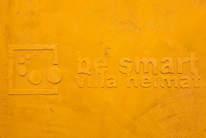 be smart villa Heimat logo als Relief an einer gelben Wand